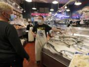 Nicholas Hartmann, center, shows a fish to a customer as he works at the Pure Food Fish Market, Tuesday, July 7, 2020, at Pike Place Market in Seattle.