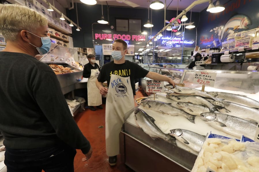 Nicholas Hartmann, center, shows a fish to a customer as he works at the Pure Food Fish Market, Tuesday, July 7, 2020, at Pike Place Market in Seattle.