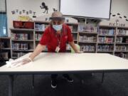 Wearing a mask and face guard as protection against the spread of COVID-19, Garland Independent School District custodian Camelia Tobon wipes down a table in the library at Stephens Elementary School in Rowlett, Texas, Wednesday, July 22, 2020.(AP Photo/LM Otero)