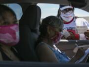 In this photo taken on Friday, June 26, 2020, Natasha Scott, right, provides flyer information about the Peacekeeper Society to Patricia Randall, center, and Floraine Gardee, left, during a drive-thru distribution of food and emergency supplies at Harrah City Hall in Harrah, Wash., during the coronavirus pandemic.