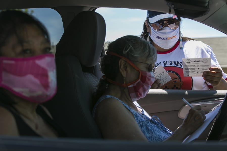 In this photo taken on Friday, June 26, 2020, Natasha Scott, right, provides flyer information about the Peacekeeper Society to Patricia Randall, center, and Floraine Gardee, left, during a drive-thru distribution of food and emergency supplies at Harrah City Hall in Harrah, Wash., during the coronavirus pandemic.