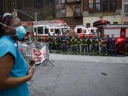 FILE - In this April 14, 2020, file photo FDNY firefighters gather to applaud medical workers as attending physician Mollie Williams, left, wears personal protective equipment due to COVID-19 concerns outside Brooklyn Hospital Center in New York. Essential workers are lauded for their service and hailed as everyday heroes. But in most states nurses, first responders and frontline workers who get COVID-19 on the job have no guarantee they&#039;ll qualify for workers&#039; comp to cover lost wages and medical care.