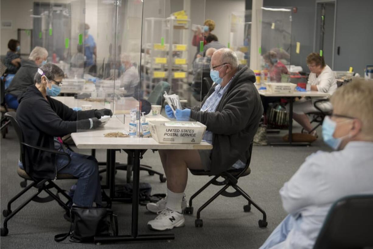 A protective panel separates Vancouver residents Gail Hinchsliff, left, and Tim Richardson as they help collect and sort ballots Tuesday morning at the Clark County Elections Office.