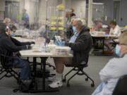 A protective panel separates Vancouver residents Gail Hinchsliff, left, and Tim Richardson as they help collect and sort ballots Tuesday morning at the Clark County Elections Office.