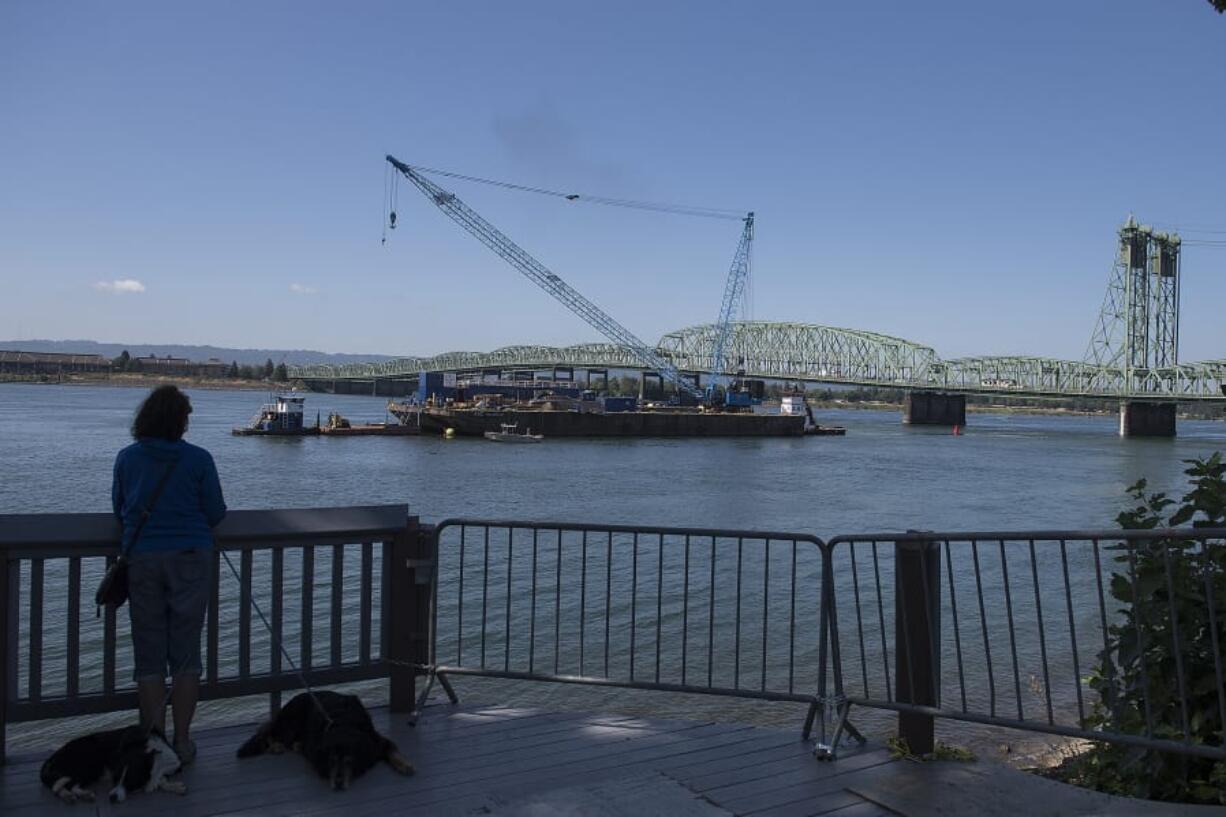 A person watches from the bank of the Columbia River as the trunnion, sheaves and other replacement components for the Interstate 5  Bridge arrive in Vancouver via barge on Tuesday morning.