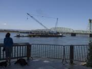 A person watches from the bank of the Columbia River as the trunnion, sheaves and other replacement components for the Interstate 5  Bridge arrive in Vancouver via barge on Tuesday morning.