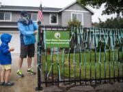 Vancouver resident Jim Mains and his son Remington, 4, tie ribbons onto the fence outside their home in Vancouver. At the end of March, Mains started this memorial for lives lost to COVID-19 in Washington. &quot;There&#039;s never been a day that we haven&#039;t put up ribbons,&quot; he said.