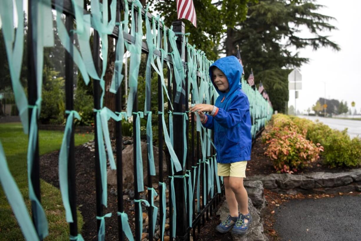 Remington Mains shakes the rain off of ribbons along the memorial outside his home in Vancouver. Each ribbon represents a life lost to COVID-19 in the state of Washington, the number now reaching more than 1,600.