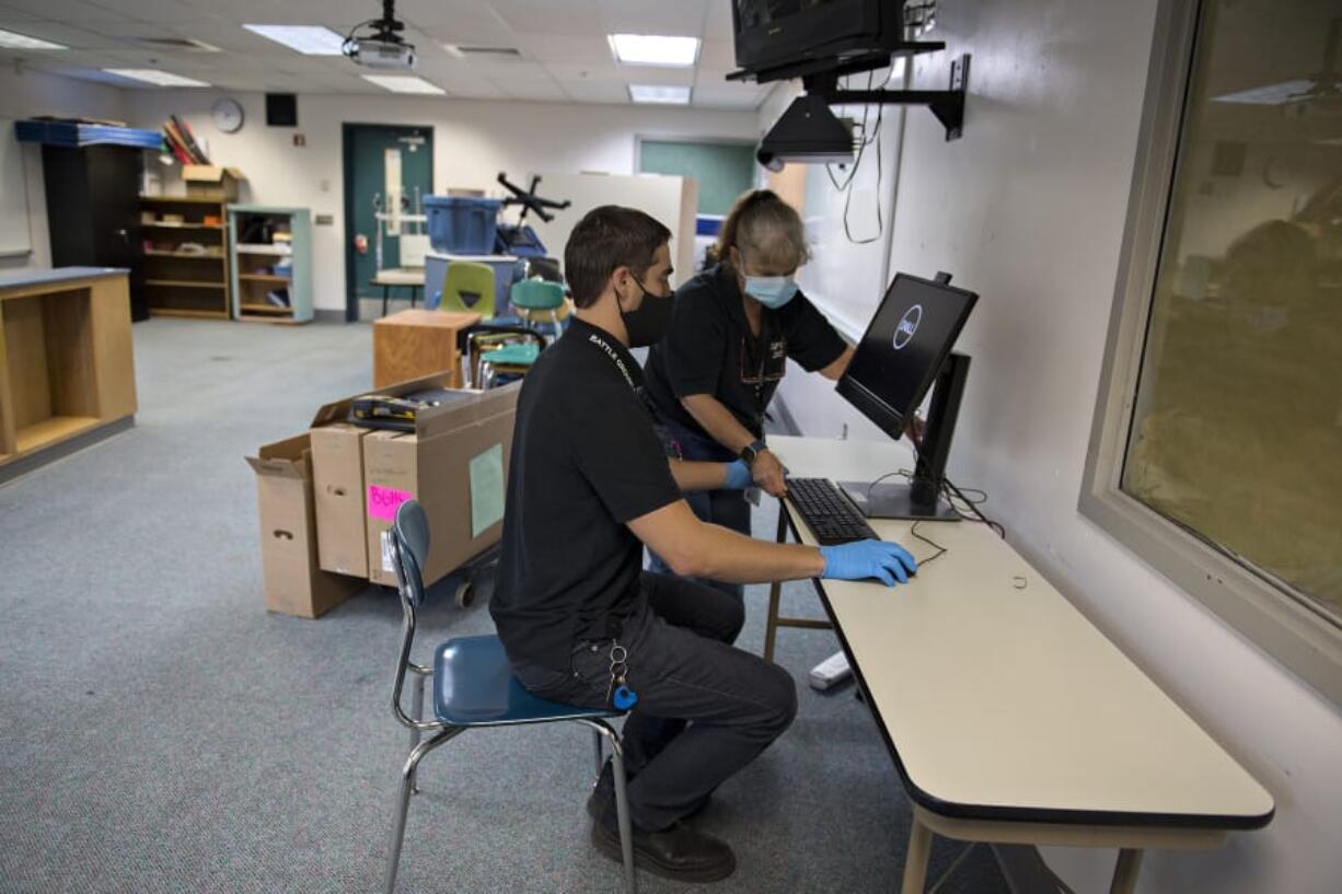 Vadim Zalyashko, left, and Jasmine John, who both work in technology services for Battle Ground Public Schools, set up a new computer to be used by a Battle Ground High School teacher remotely in the fall Tuesday morning. Clark County school districts are eligible for more than $13 million in federal coronavirus relief funds.