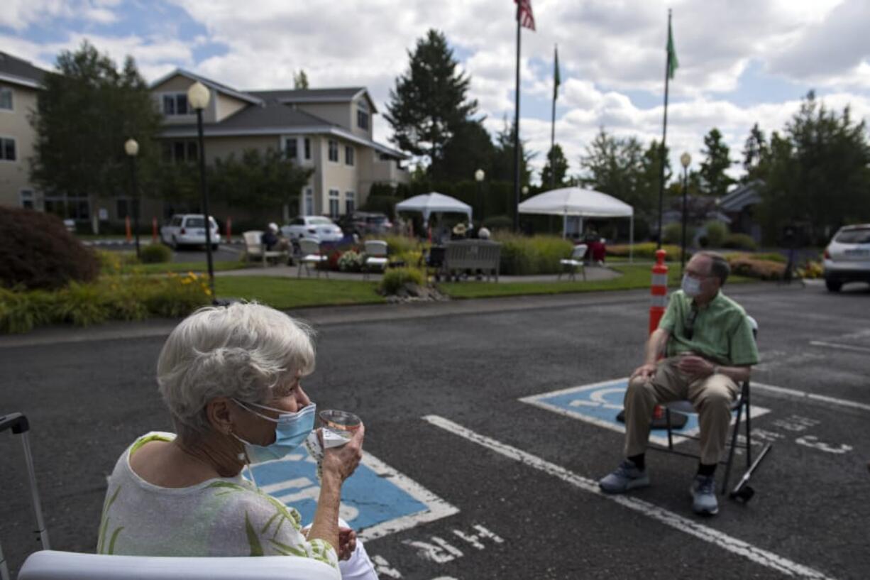 Resident Sandy Carpenter, left, practices social distancing while enjoying a glass of wine and good music with friends including Jim Etzkorn, right, during Wine Wednesday at Touchmark at Fairway Village.