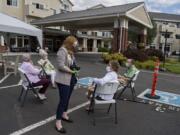 Life enrichment coordinator Moriah Leedom, center, wears a mask and face shield while chatting with resident Pat Kotson, white sweater, during Wine Wednesday at Touchmark at Fairway Village.