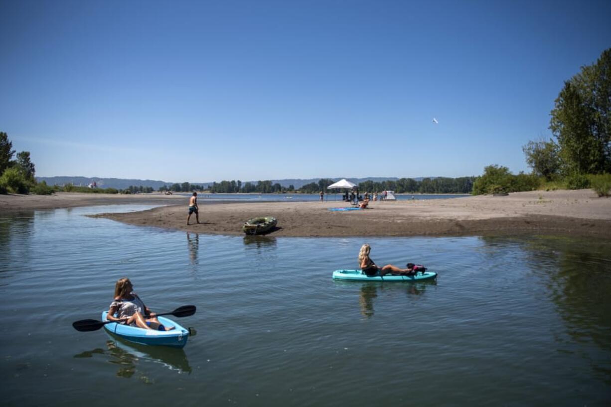 Bev Kadow, left, and her friend Kelly Kopp, right, watch an airplane fly above as they kayak along an offshoot of the Columbia River in Vancouver. An excessive-heat warning has been issued throughout the weekend until Sunday evening, with high temperatures around 100 degrees.