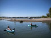 Bev Kadow, left, and her friend Kelly Kopp, right, watch an airplane fly above as they kayak along an offshoot of the Columbia River in Vancouver. An excessive-heat warning has been issued throughout the weekend until Sunday evening, with high temperatures around 100 degrees.