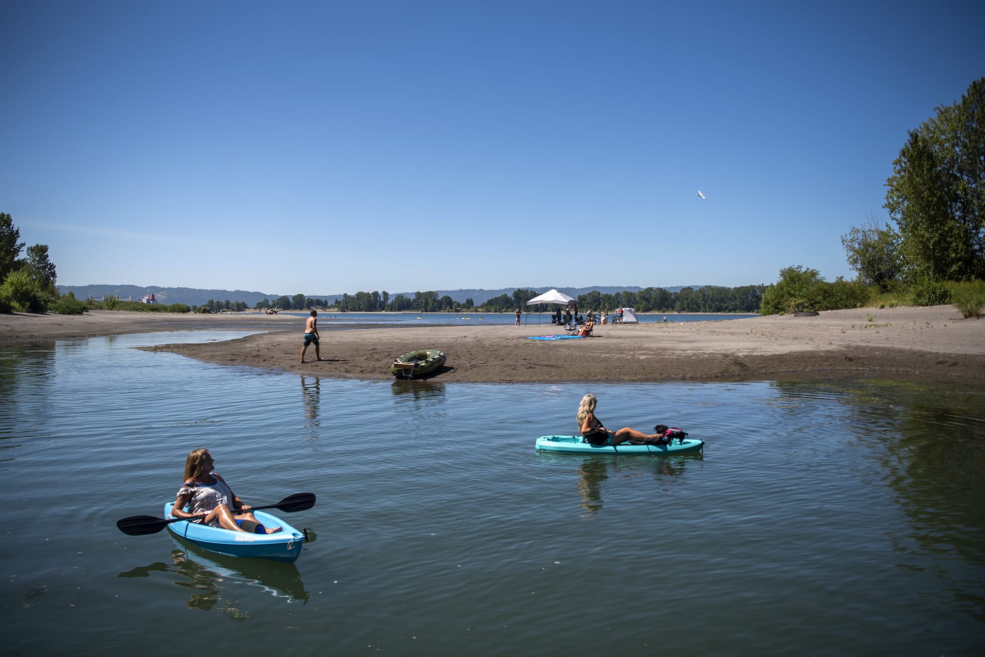 Bev Kadow, left, and her friend Kelly Kopp, right, watch an airplane fly above as they kayak along an offshoot of the Columbia River in Vancouver on August 15, 2020. An excessive heat warning has been issued throughout the weekend until Sunday evening, with temperatures around 100 degrees.
