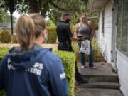 Vancouver Deputy Fire Marshal LeMont Lucas, center, shows a brief fire-safety video to Katie Jefferson outside her home Saturday morning. Firefighters and volunteers with the Vancouver Fire Department canvas Vancouver neighborhoods every week to disseminate fire safety information and hand out souvenir reminders.