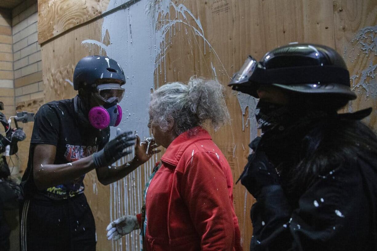 A woman who lives in a Portland neighborhood targeted by protesters argues with a few black-clad demonstrators after being splashed with white paint in front of a Portland Police Bureau precinct that was being vandalized, late Thursday, Aug. 6, 2020.