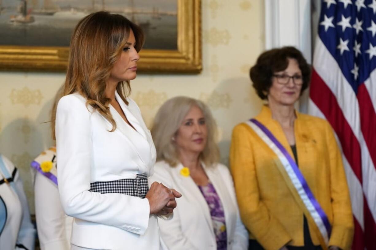 First lady Melania Trump listens as President Donald Trump speaks before signing a proclamation recognizing the 100th anniversary of the ratification of the 19th Amendment, Tuesday, Aug. 18, 2020, in the Blue Room of the White House in Washington.