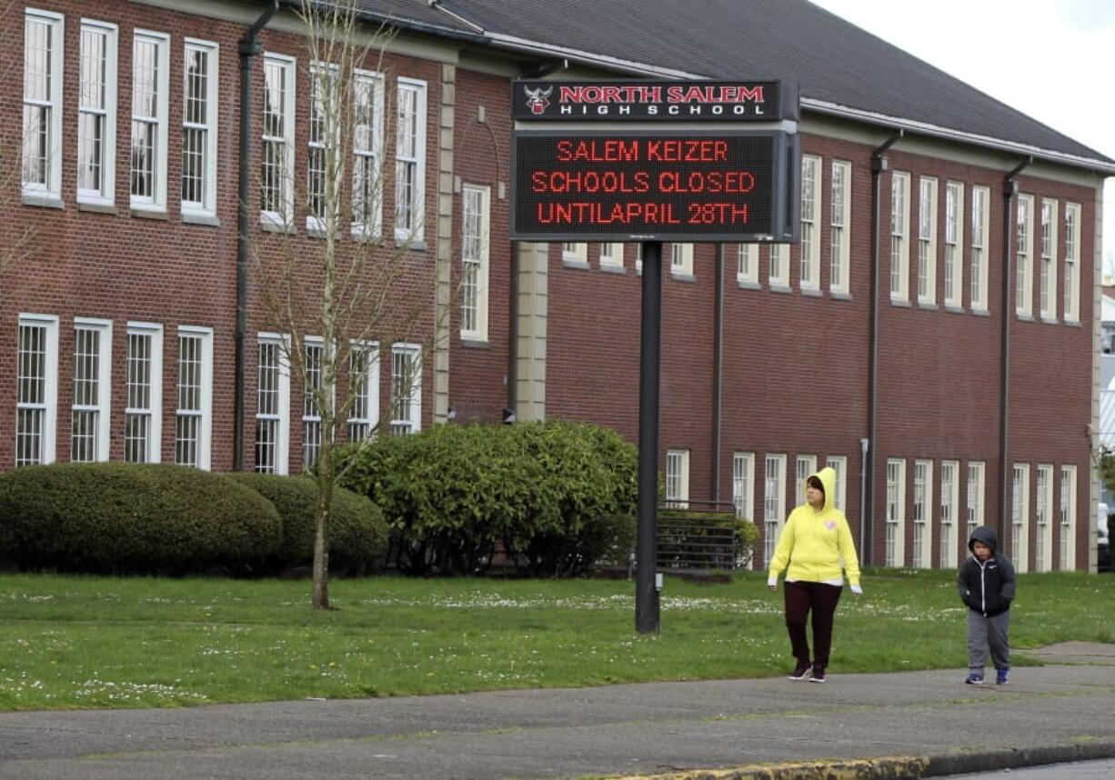 File - A woman and child walk past a North Salem High School in Salem, Ore., March 31, 2020, which like all schools in Oregon is closed because of the coronavirus. Under new COVID-19 metrics released Tuesday, July 28, 2020, students in most Oregon counties may not be able to return to their classrooms this fall, officials said.