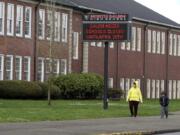 File - A woman and child walk past a North Salem High School in Salem, Ore., March 31, 2020, which like all schools in Oregon is closed because of the coronavirus. Under new COVID-19 metrics released Tuesday, July 28, 2020, students in most Oregon counties may not be able to return to their classrooms this fall, officials said.