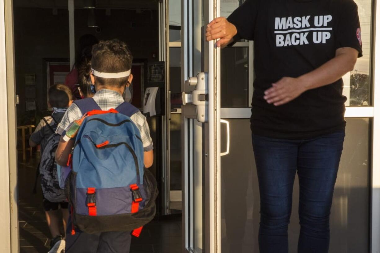 A staff member holds the door open for kids on the first day of school at Goodwin Frazier Elementary School in New Braunfels, Texas on Tuesday, Aug. 25, 2020. The number of Americans newly diagnosed with the coronavirus is falling -- a development experts credit at least partly to increased wearing of masks -- even as the outbreak continues to claim nearly 1,000 lives in the U.S. each day.