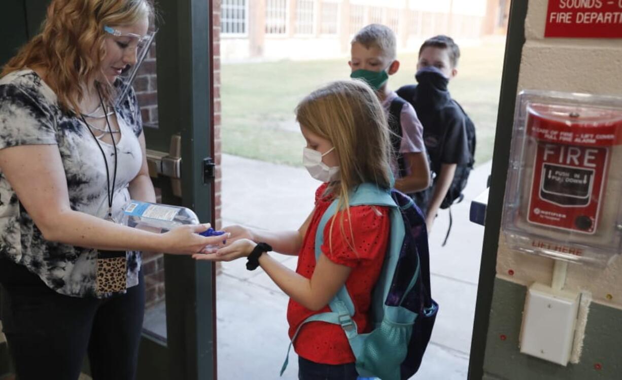 FILE - In this Aug. 5, 2020, file photo, wearing masks to prevent the spread of COVID19, elementary school students use hand sanitizer before entering school for classes in Godley, Texas. As schools reopen around the country, their ability to quickly identify and contain coronavirus outbreaks before they get out of hand is about to be put to the test.