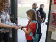 FILE - In this Aug. 5, 2020, file photo, wearing masks to prevent the spread of COVID19, elementary school students use hand sanitizer before entering school for classes in Godley, Texas. As schools reopen around the country, their ability to quickly identify and contain coronavirus outbreaks before they get out of hand is about to be put to the test.