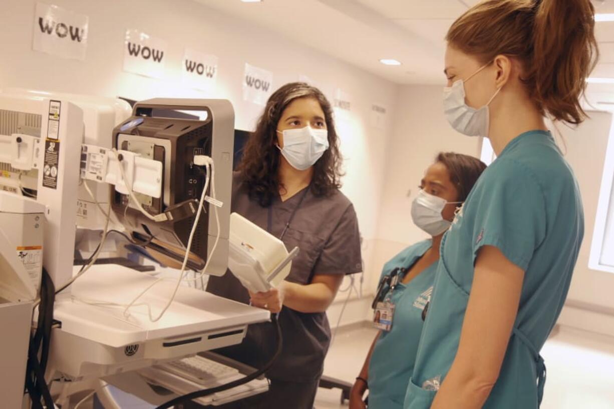 In this August 2020 photo provided by the Mount Sinai Health System, neurologist Dr. Alexandra Reynolds holds part of a device that tracks blood flow in the brain, at a hospital in New York. Reynolds was checking comatose COVID-19 patients for signs of a stroke when she stumbled onto a new clue about how the coronavirus may harm the lungs - thanks to a test that uses tiny air bubbles and a robot.