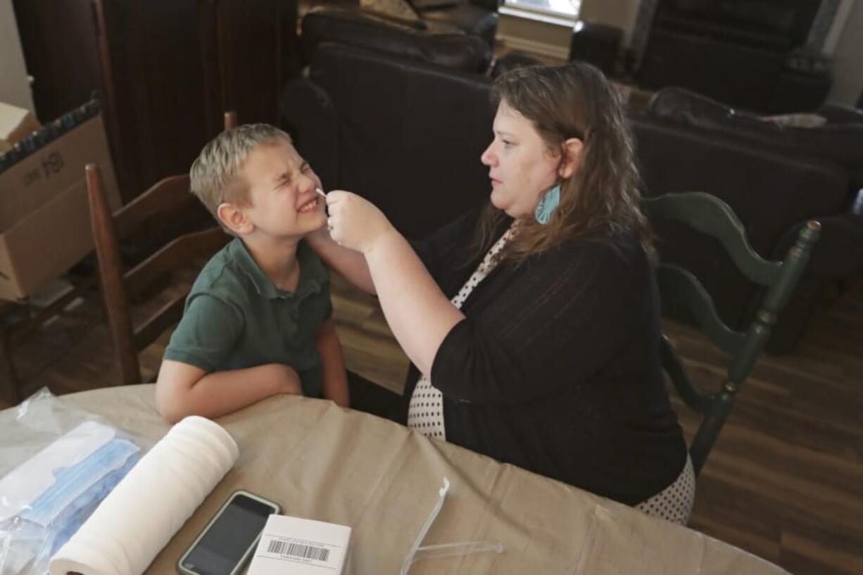 Mendy McNulty swabs the nose of her son, Andrew, 7, Tuesday, July 28, 2020, in their home in Mount Juliet, Tenn. Six thousand U.S. parents and kids are swabbing their noses twice a week to answer some of the most vexing mysteries about the coronavirus. The answers could help determine the safety of in-class education during the pandemic.