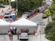 FILE - In this Sunday, July 12, 2020, vehicles wait in line at a COVID-19 testing site at the Miami Beach Convention Center during the coronavirus pandemic in Miami Beach, Fla. As coronavirus cases surge in hard-hit Florida, so do the turnaround times for test results.