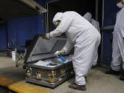 A worker wearing protective gear sprays disinfectant solution inside the coffin of a person who died from suspected COVID-19, as the body arrives Monday at the crematorium at Xilotepec Cemetery in Xochimilco, Mexico City.