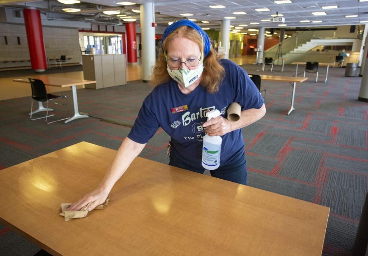 Custodial supervisor Leila Ruiz sanitizes a table in a lounge at the Compton Union Building on Friday, Aug. 28, 2020, at Washington State University in Pullman, Wash. Tables in the building are being sanitized once an hour. The university has launched the Cougs Cancel COVID campaign after a surge in the number of students testing positive for COVID-19 this week.