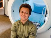 Alec Marshall poses in front of a hard-shell hyperbaric chamber at In Light Hyperbarics. The chamber is called &quot;Moby Dick&quot; because it looks like a big, white whale.