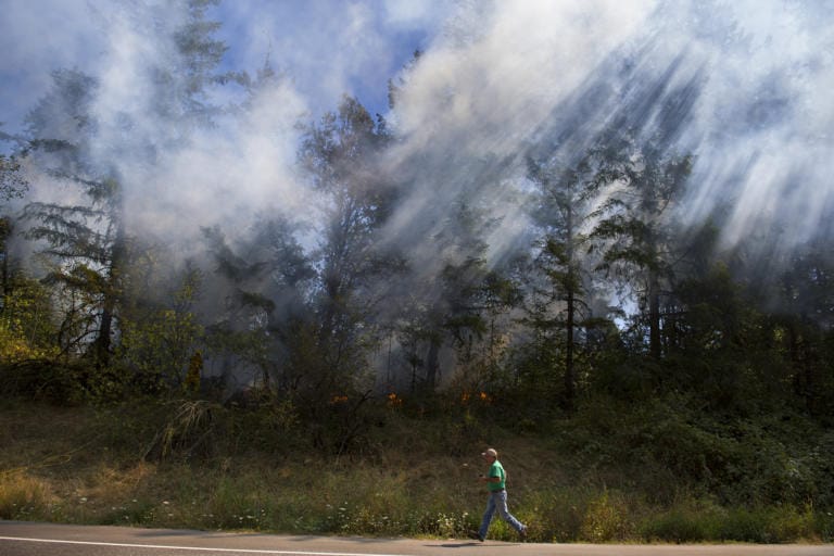 A man runs toward firefighters as sunlight illuminates smoke from a fire along Lewisville Highway on Tuesday afternoon, Sept. 8, 2020. Firefighters were called to the scene and promptly extinguished the blaze. Traffic was routed around the scene.