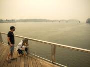 Brent McCarthy, from left, and Marissa Matthews, play on the pier Thursday at The Waterfront Vancouver with their son Xavier, 2. The family lives outside of Salem, Ore., and evacuated Tuesday to escape the smoke and fire risk. Matthews has cancer and is extra sensitive to the smoke, so although their area was still on level 2 evacuation, they decided to leave early to stay safe.