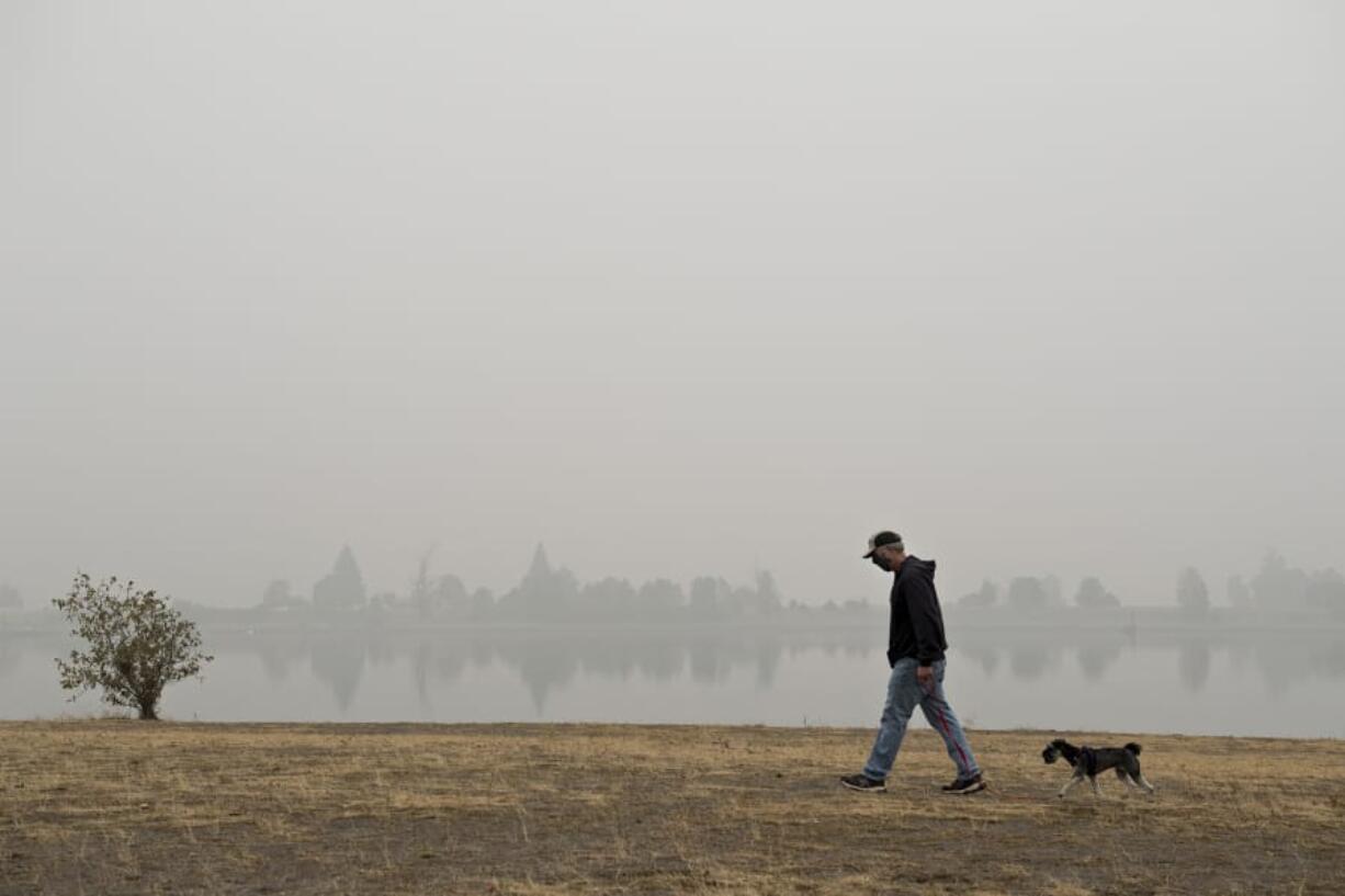 Vancouver resident Frank Schmit wears a mask while taking his dog, Ripley, a miniature schnauzer, for a stroll as thick wildfire smoke obscures the visibility of trees across the water at Frenchman' Bar Regional Park. Schmit said the fires and the smoke are just the latest in a list of unusual events that have happened in 2020. "It's been a hell of a year," he said.