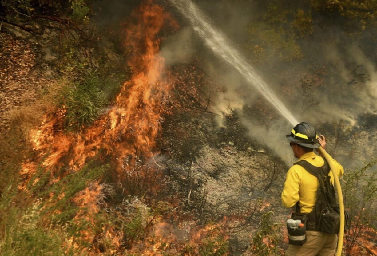 A firefighter puts out a hot spot along Highway 38 northwest of Forrest Falls, Calif., as the El Dorado Fire continues to burn Thursday afternoon, Sept. 10, 2020. The fire started by a device at a gender reveal party on Saturday.