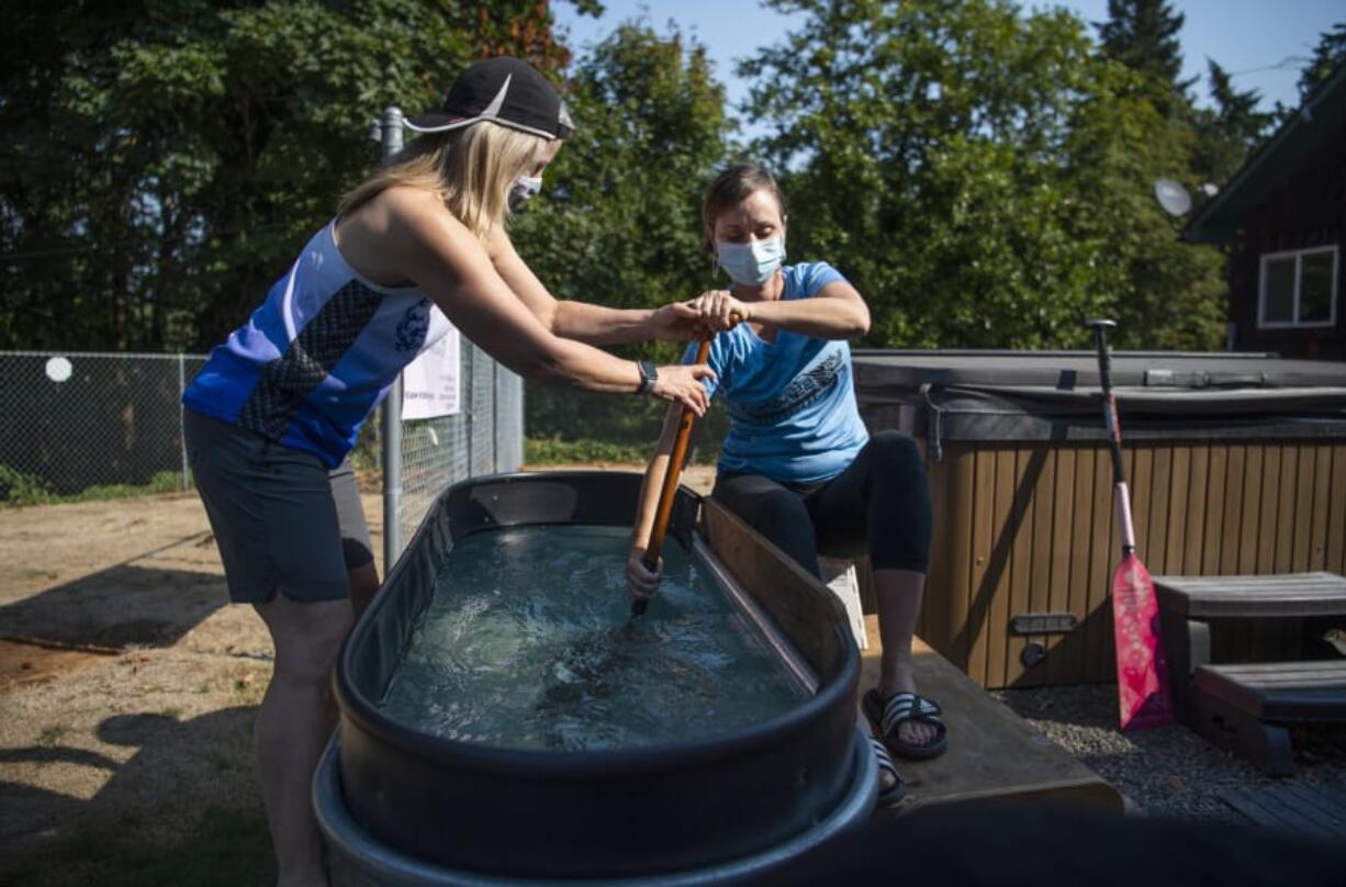 Laura Thornquist, left, demonstrates how she has been coaching teammates while the coronavirus pandemic has kept them off the lake. She corrects teammate Britten Witherspoon&#039;s form as she paddles in a water trough in Thornquist&#039;s Woodland backyard.