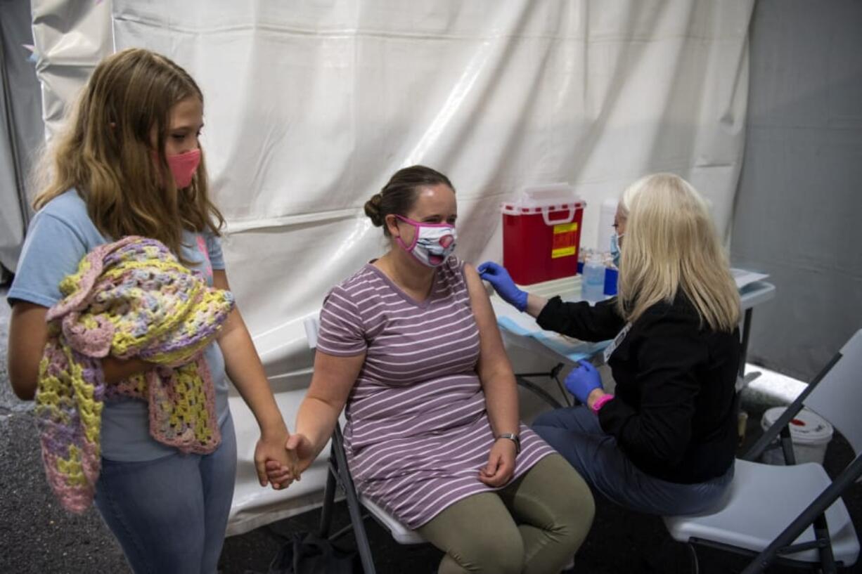 Abby Atalla, 10, comforts her mom Lara as she gets a flu shot from medical assistant Jillian Kinsella at Kaiser Permanente's Cascade Park office in Vancouver on Saturday. The office's flu shot clinic is set up in an outdoor tent in order to maintain safe social distancing due to the COVID-19 pandemic.