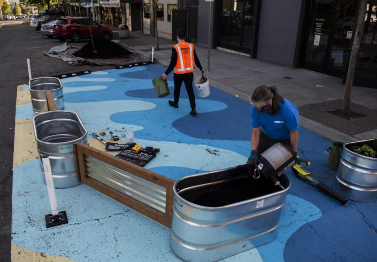 Michael Walker, executive director of Vancouver&#039;s Downtown Association, left, and executive assistant Melodi Ramquist fill shiny planters with potting soil in the new &quot;parklet&quot; on the street outside The Source Climbing Center.