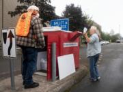 Vancouver resident Sharon Grammar, right, drops off her ballot while elections worker John Waterbury collects ballots from an official ballot drop box near the Clark County Elections Office in downtown Vancouver on Saturday morning.