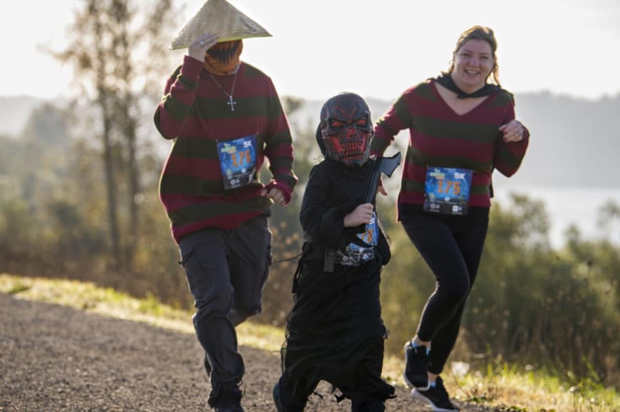 Joey Catania, from left, runs alongside 7-year-old Maxx Catania and Crystal Catania in WhyRacingis Scary Run on Saturday morning, October 31, 2020, in Washougal. Roughly 300 runners, many costumed, enjoyed a sunny morning along the Columbia River taking part in the family-friendly event, which featured 5- and 10-kilometer courses and a half marathon.