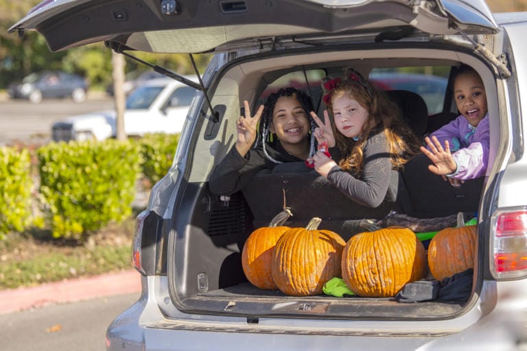 Kaia Silva, 11, from left, Juliann Galey, 9, and Leilani Quint, 9, smile and wave at the camera while looking out the back of an SUV as part of fourth annual Booville, a drive-through Halloween event put on by the Parks Foundation of Clark County at Vancouver Mall on Saturday.