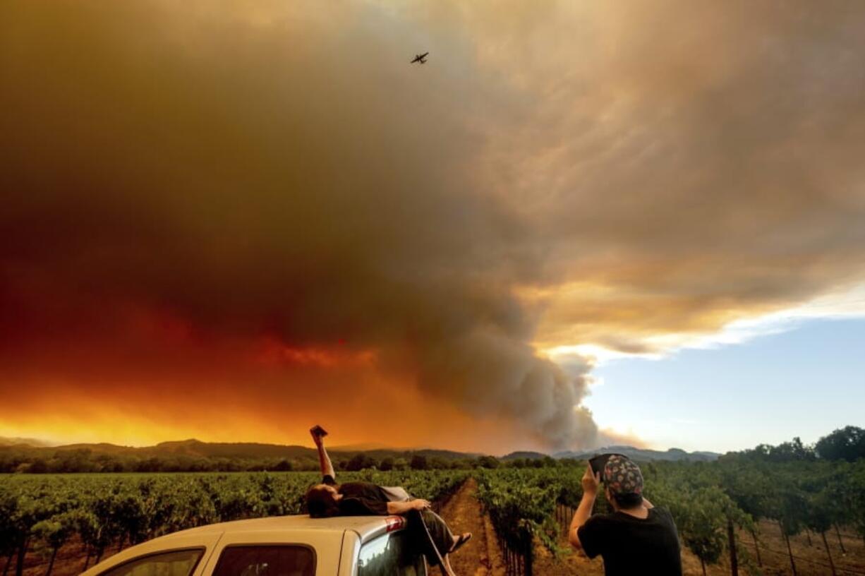 FILE - In this Thursday, Aug. 20, 2020, file photo, Thomas Henney, left, and Charles Chavira watch a plume spread over Healdsburg, Calif., as the LNU Lightning Complex fires burn. Deadly wildfires in California have burned more than 4 million acres (6,250 square miles) this year -- more than double the previous record for the most land burned in a single year in the state. California fire officials said the state hit the astonishing milestone Sunday, Oct. 4, 2020 with about two months remaining in the fire season.