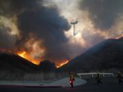 A helicopter drops water as firefighters walk with drip torches to set a backfire against the Blue Ridge Fire on Tuesday, Oct. 27, 2020, in Chino Hills, Calif. Facing extreme wildfire conditions this week that included hurricane-level winds, the main utility in Northern California cut power to nearly 1 million people while its counterpart in Southern California pulled the plug on just 30 customers to prevent power lines and other electrical equipment from sparking a blaze. (AP Photo/Jae C.