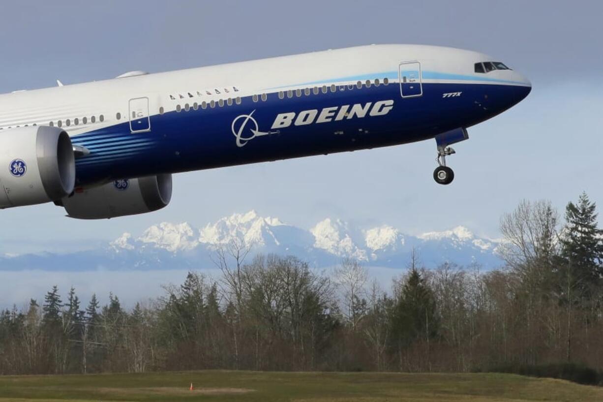 FILE - In this Jan. 25, 2020, file photo a Boeing 777X airplane takes off on its first flight with the Olympic Mountains in the background at Paine Field in Everett, Wash.  Boeing will cut more jobs as it continues to lose money and revenue during a pandemic that has smothered demand for new airline planes. The company said Wednesday, Oct. 28,  that it expects to cut its workforce to about 130,000 employees by the end of next year, down 30,000 from the start of this year.  (AP Photo/Ted S.