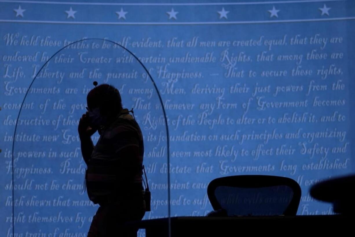 A member of the production crew walks behind a glass panel on stage which will serve as a barrier to protect the spread of COVID-19 as preparations take place for the vice presidential debate at the University of Utah, Tuesday, Oct. 6, 2020, in Salt Lake City. The vice presidential debate between Vice President Mike Pence and Democratic vice presidential candidate, Sen. Kamala Harris, D-Calif., is scheduled for Oct. 7.