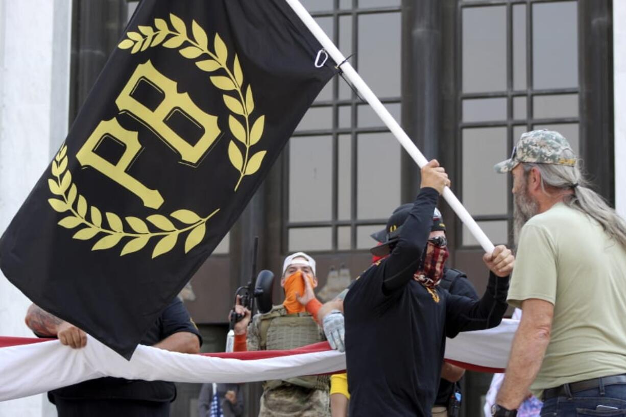 FILE - In this Sept. 7, 2020 photo, a protester carries a Proud Boys banner, symbol of a right-wing group, while other members start to unfurl a large U.S. flag in front of the Oregon State Capitol in Salem, Ore. President Donald Trump didn&#039;t condemn white supremacist groups and their role in violence in some American cities this summer. Instead, he said the violence is a &quot;left-wing&quot; problem and he told one far-right extremist group to &quot;stand back and stand by.&quot; His comments Tuesday night were in response to debate moderator Chris Wallace asking if he would condemn white supremacists and militia groups. Trump&#039;s exchange with Democrat Joe Biden left the extremist group Proud Boys celebrating what some of its members saw as tacit approval.