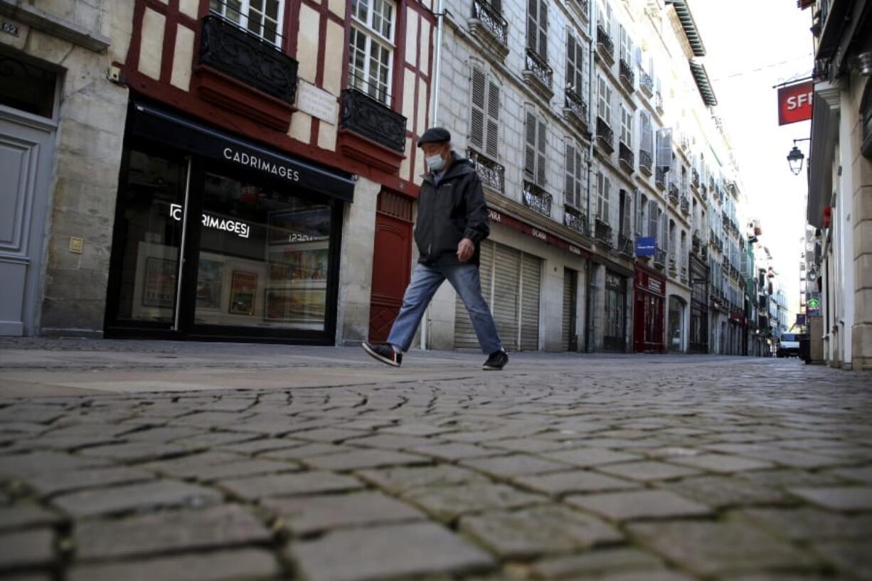 A man walks in an empty street during a nationwide confinement to counter the Covid-19, in Bayonne, southwestern France Friday, Oct. 30, 2020 . France re-imposed a monthlong nationwide lockdown Friday aimed at slowing the spread of the virus, closing all non-essential business and forbidding people from going beyond one kilometer from their homes except to go to school or a few other essential reasons.