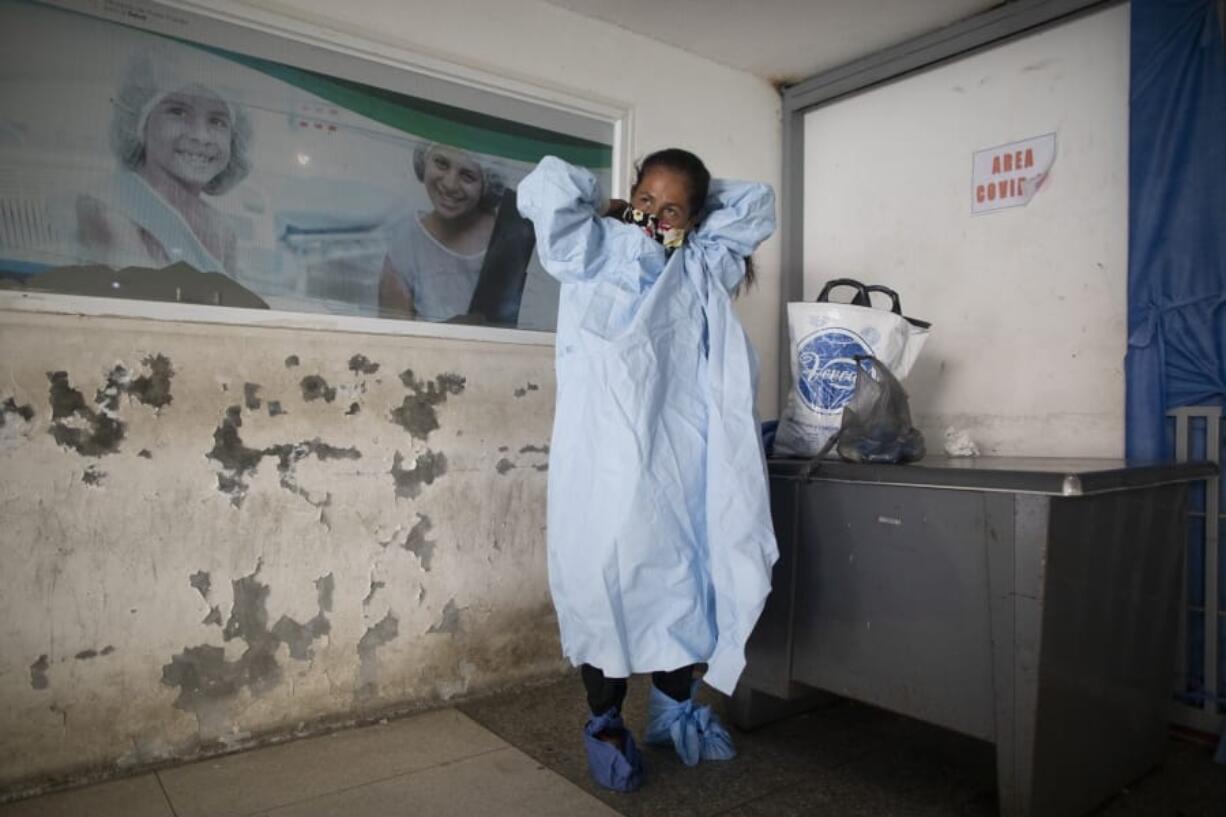 Elena Suazo, a kindergarten cafeteria worker, puts on the protective gear she brought from home, outside the entrance to the COVID-19 wing of Jose Gregorio Hernandez Hospital which used to be the emergency room, as she prepares to enter and care for her 76-year-old hospitalized father, in the Catia neighborhood of Caracas, Venezuela, Thursday, Sept. 24, 2020. In this ruined country, the only way to ensure that he received the care he needed was to do it herself, regardless of the dangers to her own health.