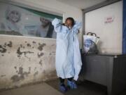 Elena Suazo, a kindergarten cafeteria worker, puts on the protective gear she brought from home, outside the entrance to the COVID-19 wing of Jose Gregorio Hernandez Hospital which used to be the emergency room, as she prepares to enter and care for her 76-year-old hospitalized father, in the Catia neighborhood of Caracas, Venezuela, Thursday, Sept. 24, 2020. In this ruined country, the only way to ensure that he received the care he needed was to do it herself, regardless of the dangers to her own health.